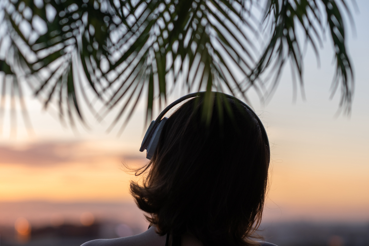 Une femme aux cheveux court se tient de dos, casque sur la tête et regarde le soleil se coucher 