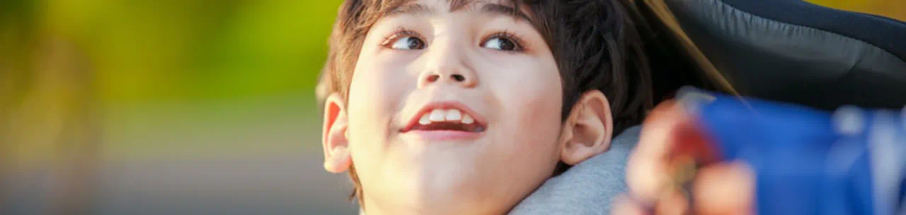 Un enfant en fauteuil roulant lève les yeux vers son proche et sourit.