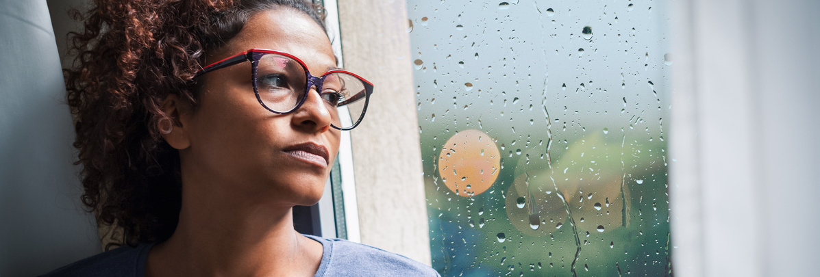 Une femme d'une quarantaine d'années regarde la pluie tomber par la fenêtre avec un air inquiet