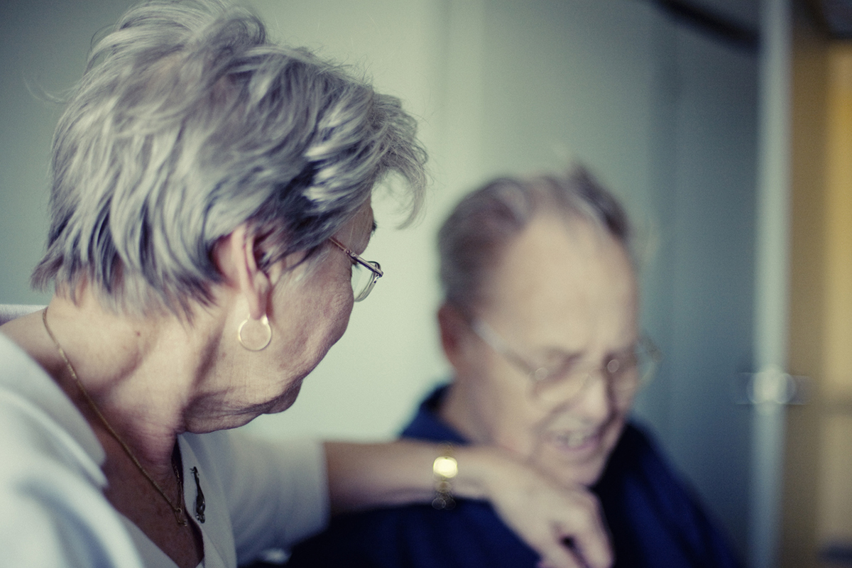 Une femme est tournée vers son mari, la main sur son épaule, lors de son départ en établissement de retraite.