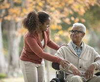 Un adulte handicapé en fauteuil roulant sourit à la jeune femme qui l'accompagne en balade.