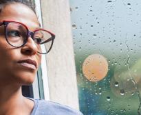 Une femme d'une quarantaine d'années regarde la pluie tomber par la fenêtre avec un air inquiet