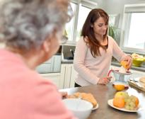 Une jeune femme en congé proche aidant prépare un jus d'orange maison pour sa grand-mère