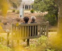 Une femme est assise auprès de sa mère gravement malade, de dos, sur un banc face à un parc.