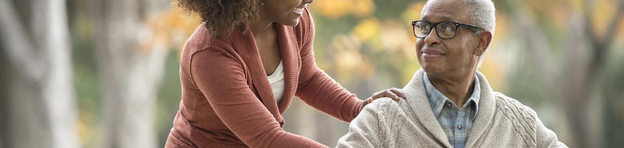 Un adulte handicapé en fauteuil roulant sourit à la jeune femme qui l'accompagne en balade.