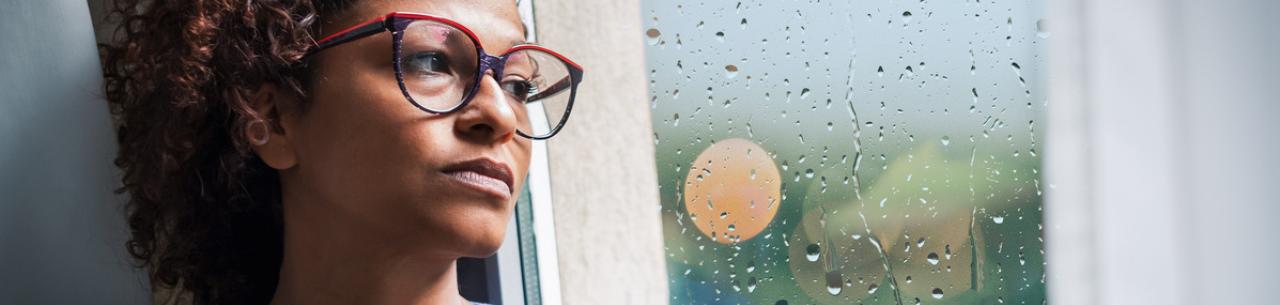 Une femme d'une quarantaine d'années regarde la pluie tomber par la fenêtre avec un air inquiet