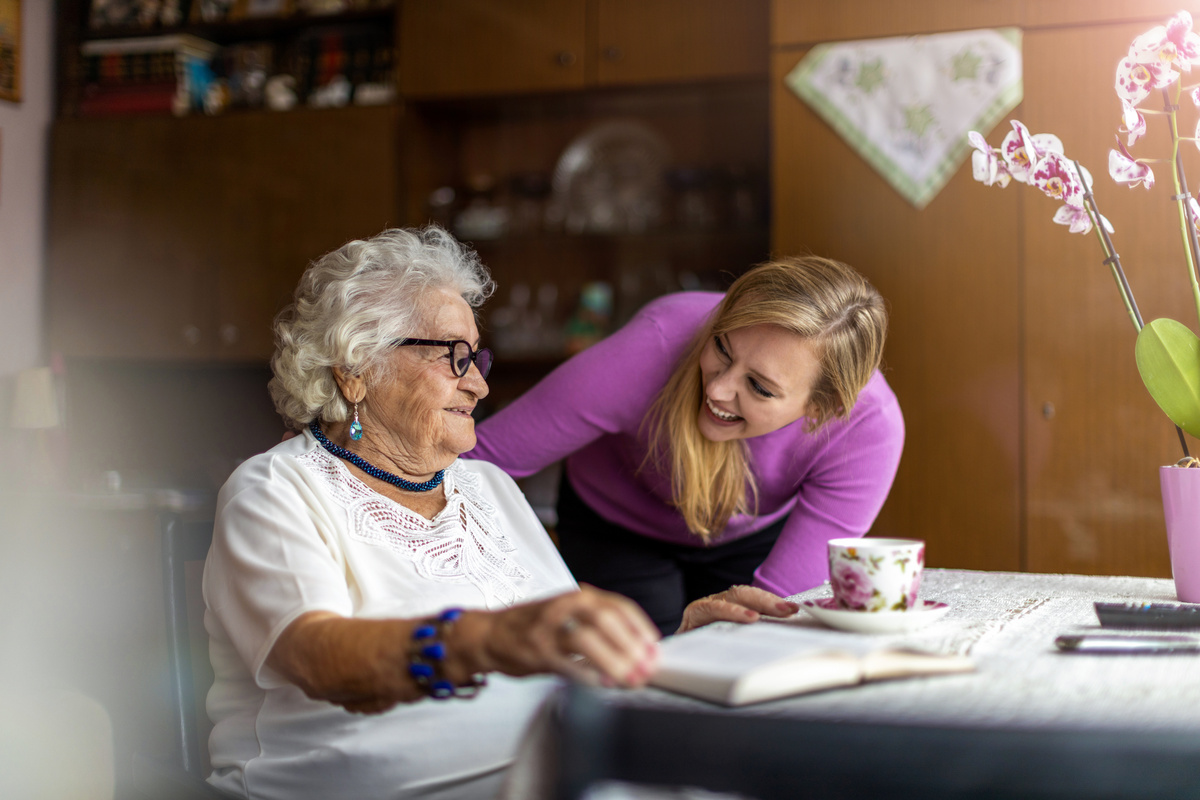 Une jeune femme aide à domicile rigole avec une dame âgée 