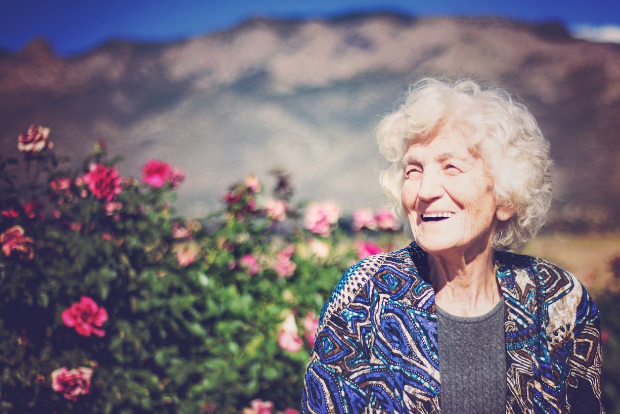 Une femme âgée devant un buisson fleurit 