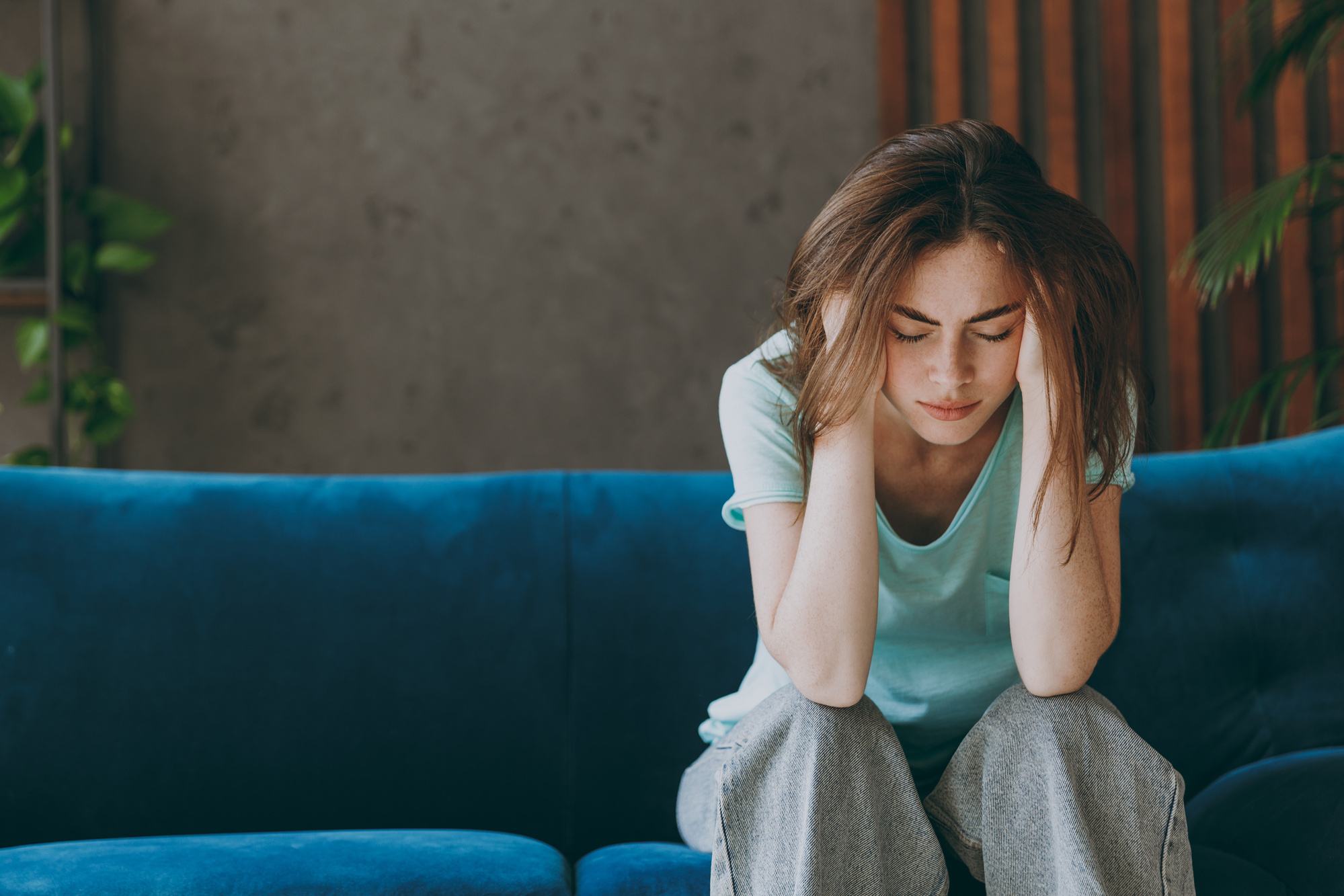 Une jeune femme brune est assise sur un canapé, elle se masse la tempe, fatiguée par l'accompagnement de son proche